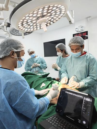 Operative photograph of a team using overhead surgical lights and ultrasound over a draped field. The patient's face is not shown.