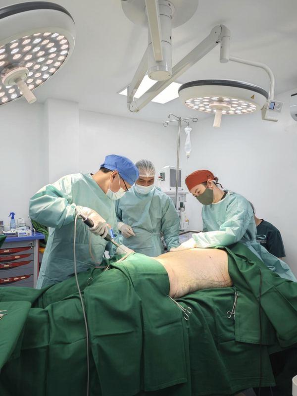 Operative photograph of a body-contouring case under twin LED surgical lights at Center for Advanced Aesthetics, Quezon City. The patient's face is not shown.